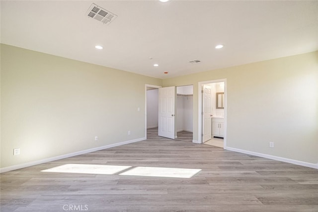 unfurnished bedroom with ensuite bath, a walk in closet, and light hardwood / wood-style floors