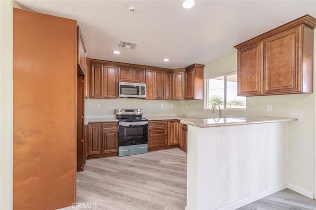 kitchen with light hardwood / wood-style floors, kitchen peninsula, and appliances with stainless steel finishes