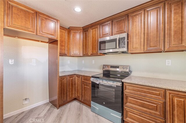 kitchen featuring light stone counters, light hardwood / wood-style flooring, a textured ceiling, and appliances with stainless steel finishes