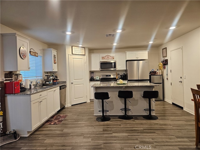 kitchen featuring stone counters, a center island, appliances with stainless steel finishes, and dark hardwood / wood-style floors