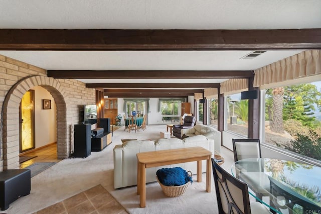 carpeted living room featuring beam ceiling and brick wall