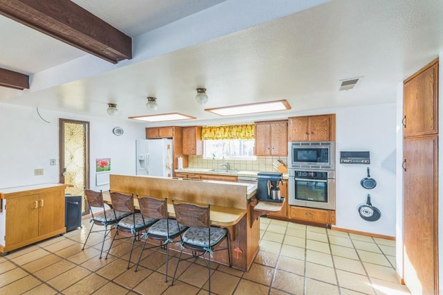 kitchen with backsplash, light tile patterned floors, beamed ceiling, sink, and stainless steel appliances