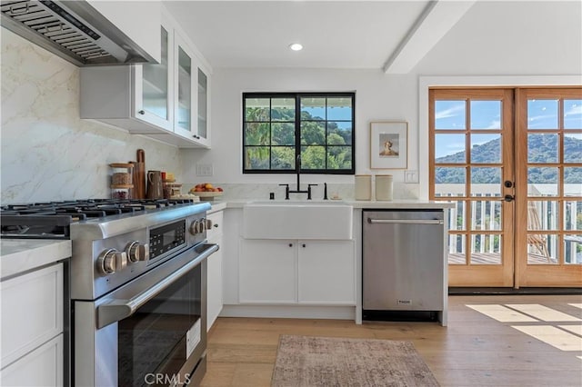 kitchen featuring white cabinetry, light hardwood / wood-style flooring, wall chimney exhaust hood, and appliances with stainless steel finishes