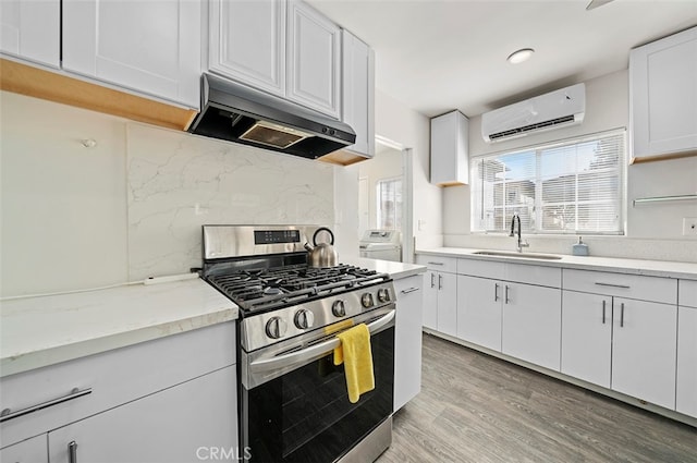 kitchen with sink, gas stove, a wall mounted AC, ventilation hood, and white cabinets