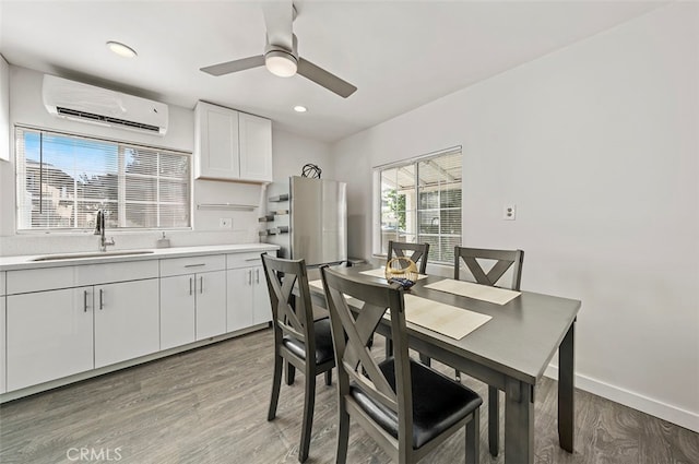 dining space with a wall unit AC, sink, hardwood / wood-style flooring, and ceiling fan