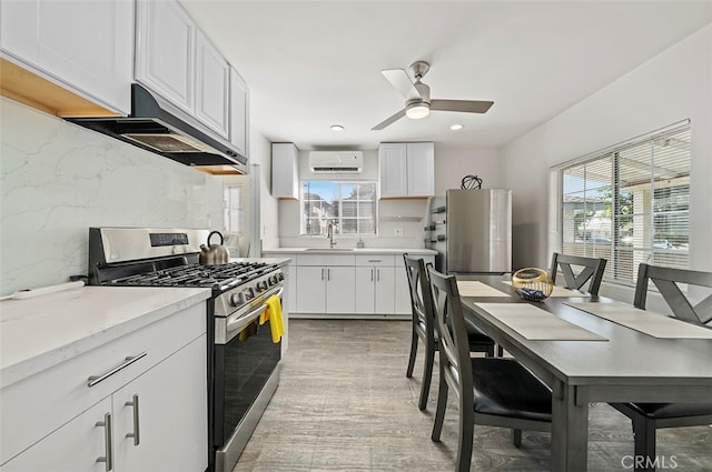 kitchen with stainless steel appliances, ceiling fan, ventilation hood, white cabinets, and decorative backsplash