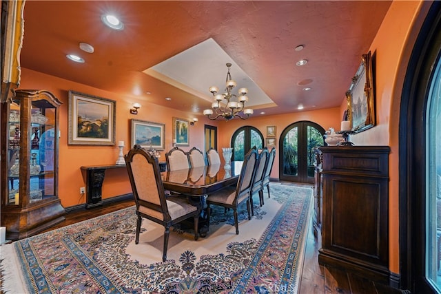 dining space featuring wood-type flooring, french doors, a tray ceiling, and a chandelier