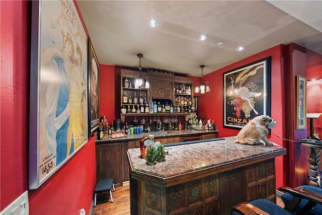 bar with decorative light fixtures, sink, dark stone counters, light wood-type flooring, and dark brown cabinets