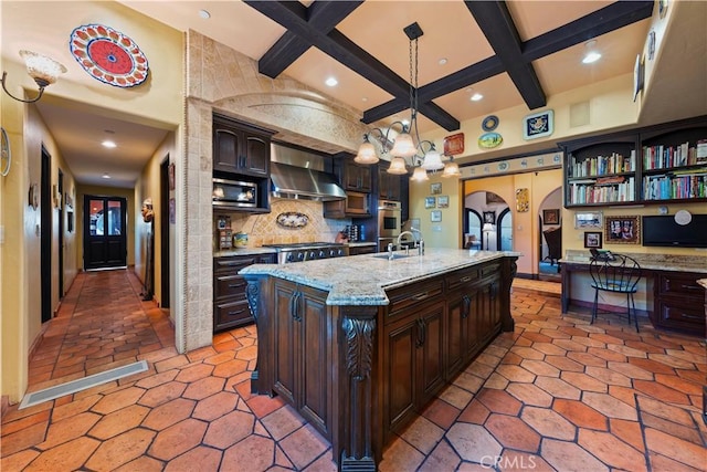 kitchen with a center island with sink, tasteful backsplash, wall chimney range hood, pendant lighting, and dark brown cabinetry