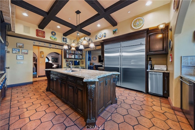 kitchen with pendant lighting, stainless steel built in fridge, dark brown cabinets, and an island with sink