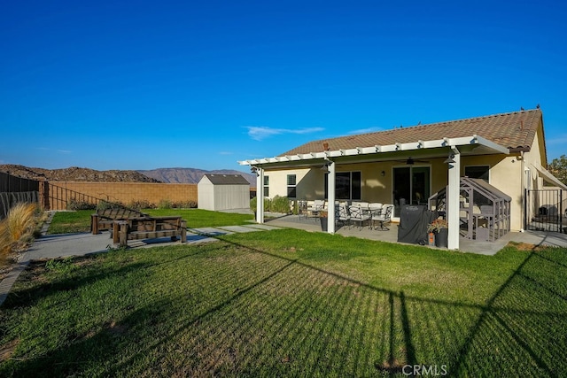 rear view of property with ceiling fan, a storage unit, a yard, a patio, and a mountain view