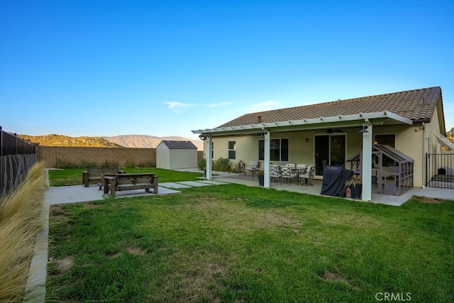 rear view of house featuring a yard, a mountain view, a shed, a patio, and ceiling fan