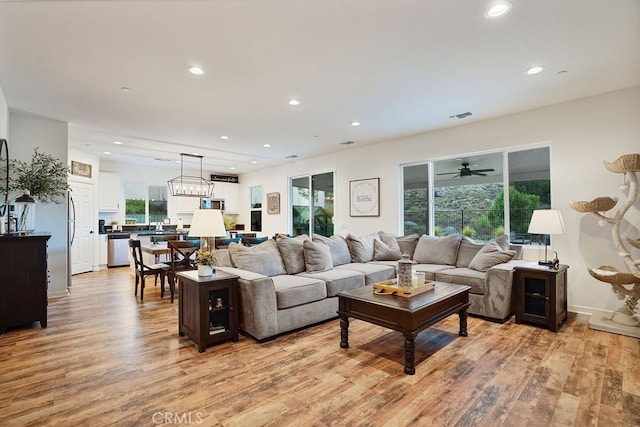 living room with ceiling fan with notable chandelier and light hardwood / wood-style floors