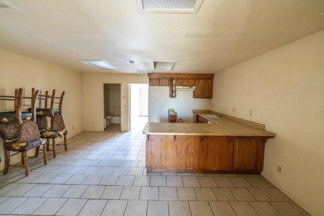 kitchen with kitchen peninsula, a breakfast bar area, light tile patterned floors, a textured ceiling, and sink