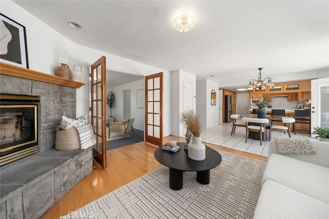 living room with a fireplace, french doors, an inviting chandelier, and light wood-type flooring