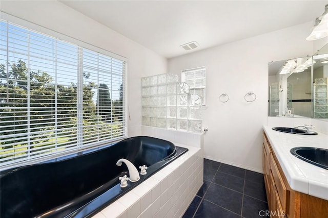 bathroom with tile patterned floors, tiled tub, vanity, and a healthy amount of sunlight