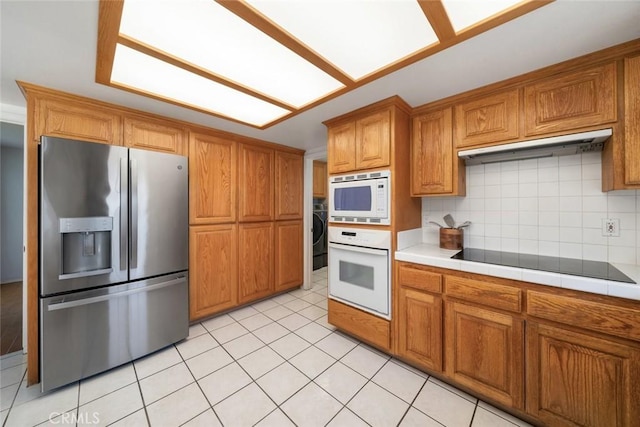 kitchen with tasteful backsplash, tile countertops, light tile patterned floors, and white appliances