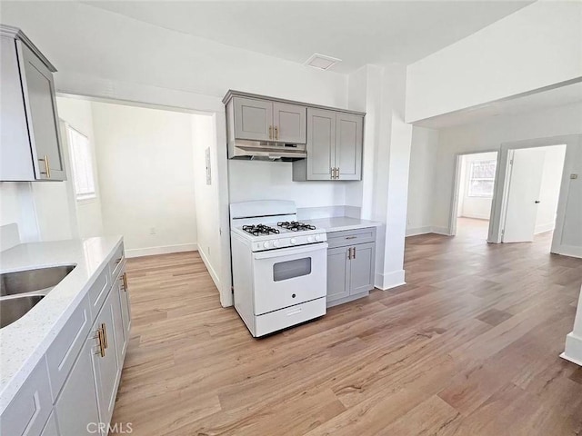 kitchen featuring white range with gas stovetop, sink, light hardwood / wood-style flooring, and gray cabinetry