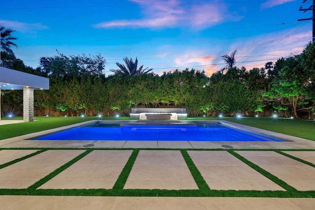 pool at dusk featuring a patio area, a yard, and a jacuzzi