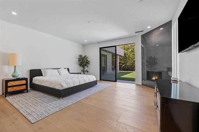 bedroom featuring access to exterior, light wood-type flooring, and a high end fireplace