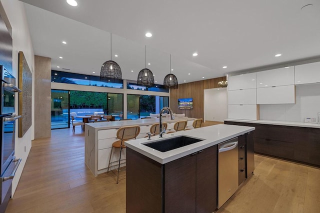 kitchen featuring dark brown cabinetry, sink, white cabinets, hanging light fixtures, and an island with sink