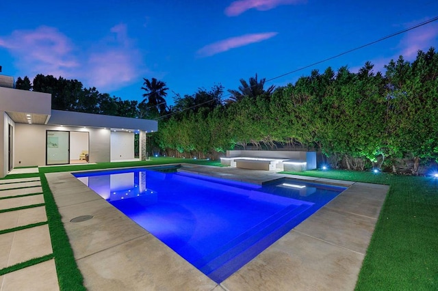 pool at dusk featuring a hot tub