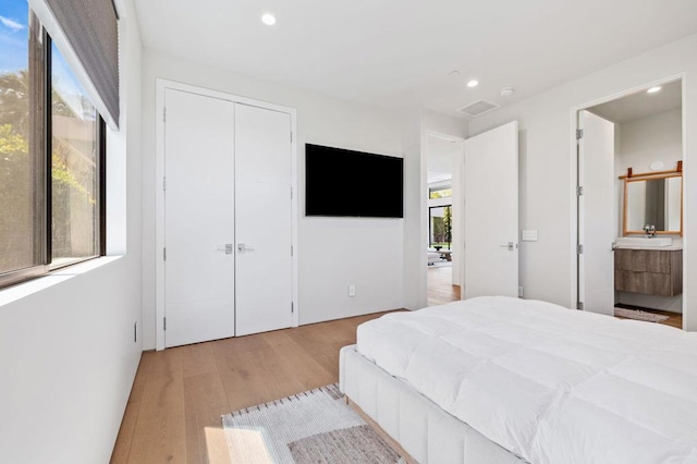 bedroom featuring light wood-type flooring, sink, connected bathroom, and a closet