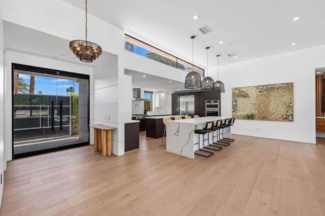 kitchen featuring wall chimney exhaust hood, a chandelier, a spacious island, decorative light fixtures, and light hardwood / wood-style floors