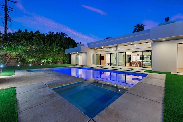 pool at dusk with an in ground hot tub and a patio