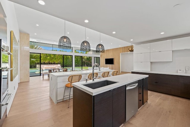 kitchen with dark brown cabinetry, sink, white cabinetry, hanging light fixtures, and an island with sink