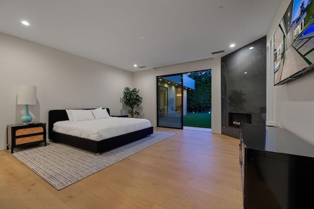 bedroom with access to exterior, light wood-type flooring, and a fireplace