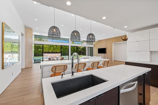 kitchen featuring light wood-type flooring, sink, pendant lighting, dishwasher, and white cabinetry