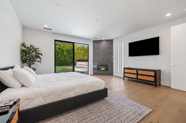 bedroom featuring access to outside, a large fireplace, and light hardwood / wood-style flooring