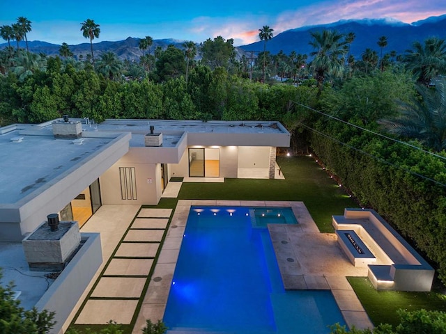 pool at dusk with a lawn, a mountain view, and a patio area