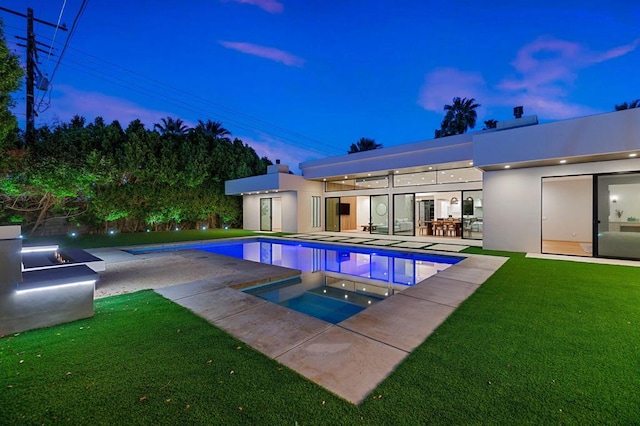 pool at dusk featuring a patio area, an in ground hot tub, and a yard