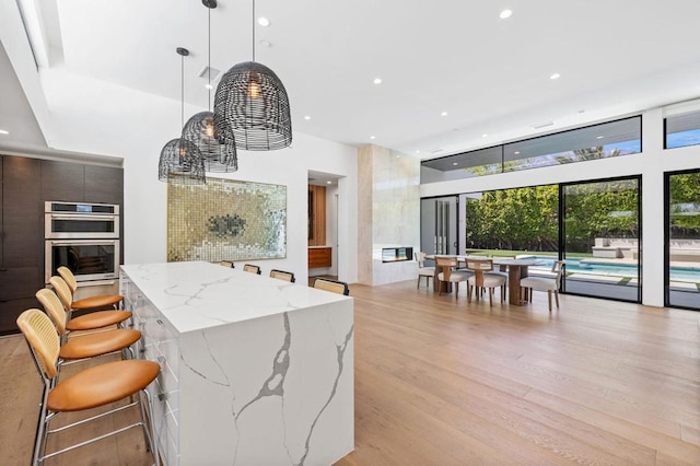 kitchen featuring a kitchen breakfast bar, light stone counters, double oven, light hardwood / wood-style floors, and decorative light fixtures