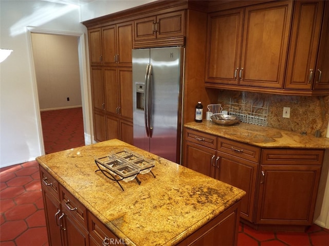 kitchen featuring light stone countertops, a center island, tasteful backsplash, dark tile patterned floors, and stainless steel refrigerator with ice dispenser