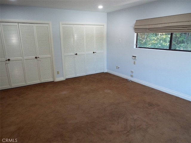 unfurnished bedroom with two closets and dark colored carpet