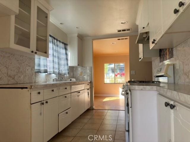 kitchen with decorative backsplash, white gas range oven, crown molding, light tile patterned floors, and white cabinetry