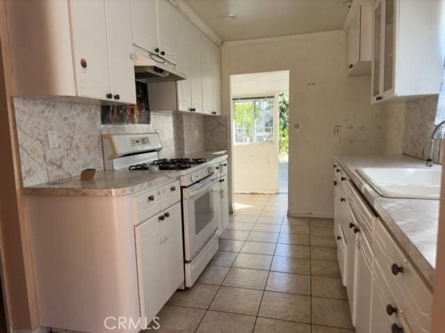 kitchen with gas range gas stove, sink, light tile patterned floors, backsplash, and white cabinets