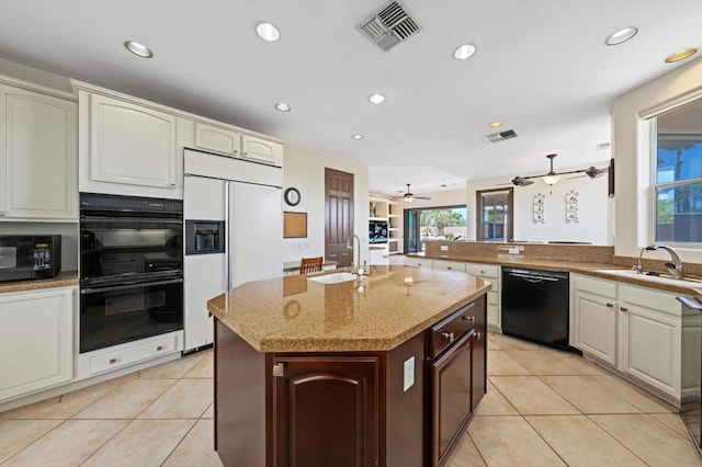 kitchen with sink, light tile patterned floors, black appliances, and a center island with sink