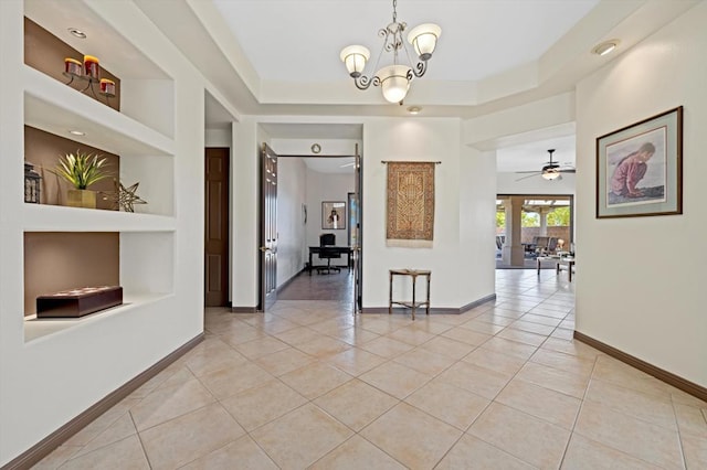 corridor featuring a raised ceiling, built in features, light tile patterned flooring, and an inviting chandelier