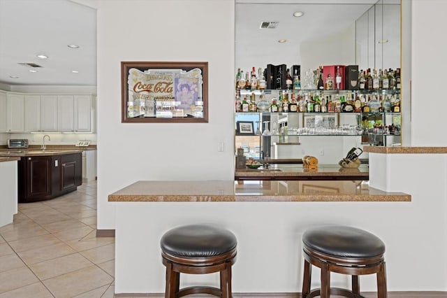 bar with white cabinets, light tile patterned floors, dark brown cabinets, and sink