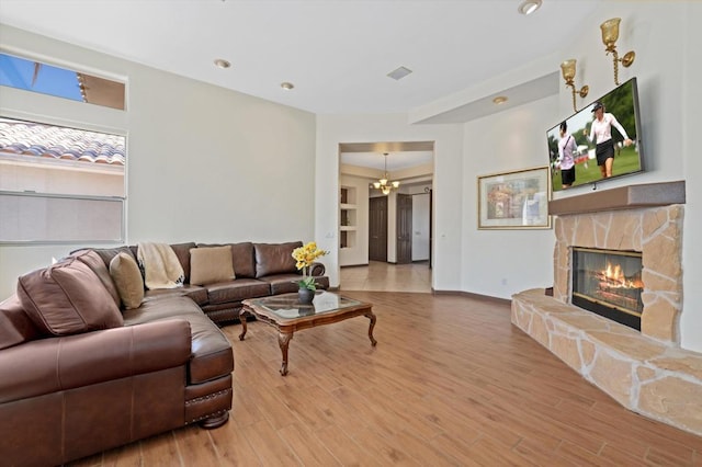 living room featuring hardwood / wood-style floors, a notable chandelier, and a stone fireplace