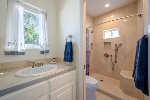 bathroom with a tile shower, vanity, toilet, and a healthy amount of sunlight