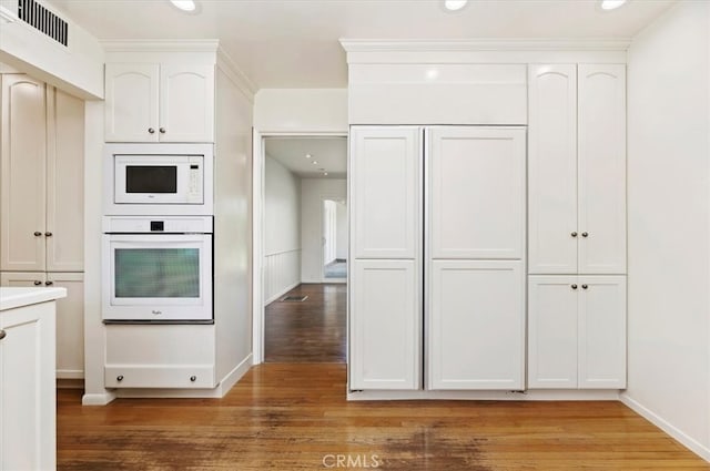 kitchen with white cabinetry, wood-type flooring, and white appliances