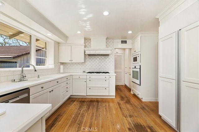 kitchen with decorative backsplash, hardwood / wood-style floors, white cabinets, sink, and white appliances