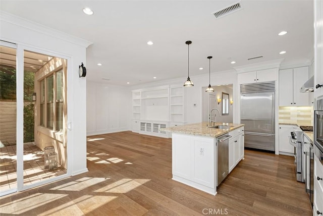 kitchen with hanging light fixtures, premium appliances, light hardwood / wood-style flooring, an island with sink, and white cabinets