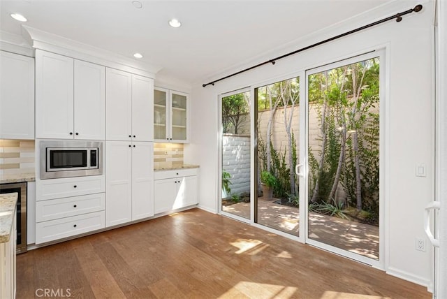 kitchen with hardwood / wood-style floors, stainless steel microwave, white cabinets, decorative backsplash, and light stone counters