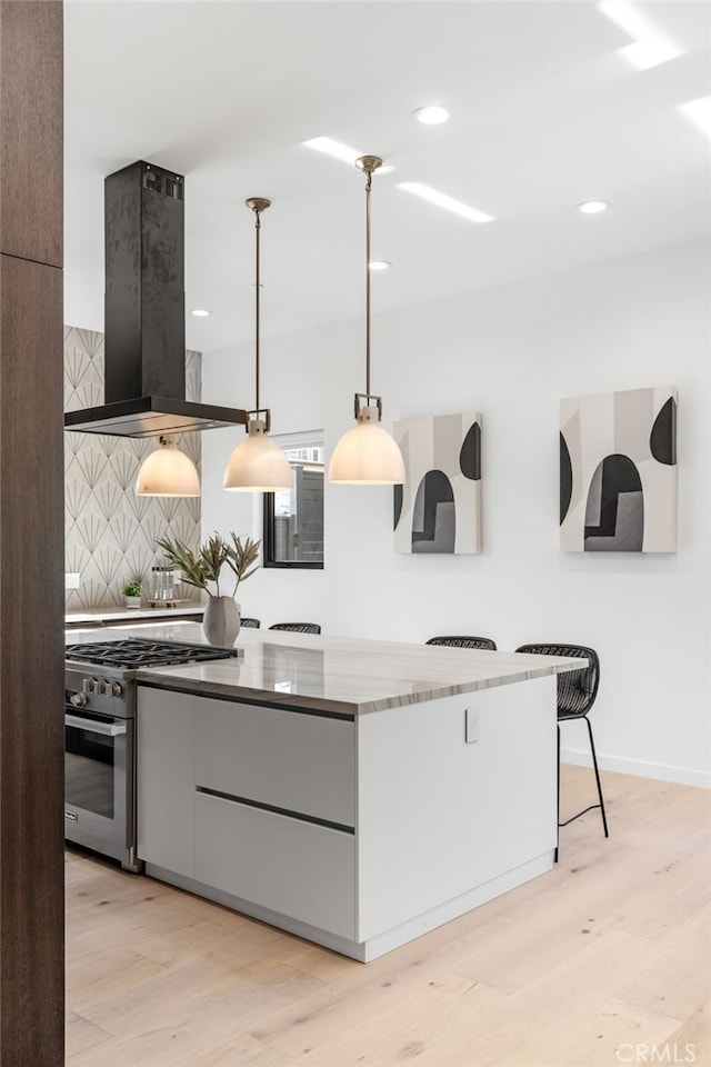 kitchen with pendant lighting, ventilation hood, high end stainless steel range oven, light wood-type flooring, and tasteful backsplash